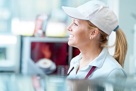 a girl with a uniform and hat on stands behind a fast-food counter