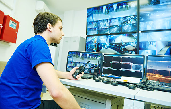 A man looks at multiple video screens displaying CCTV video surveillance.