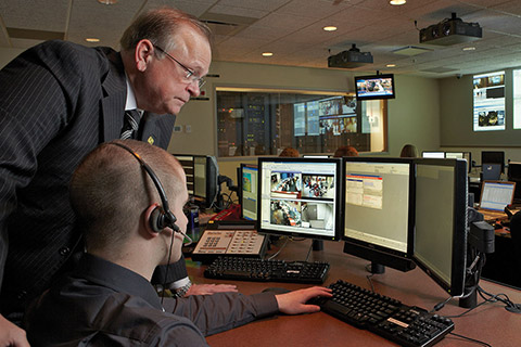 Mike Neugebauer, VP and Director of Corporate Security for Fifth Third Bank, leans over a man sitting at a computer monitor to view video surveillance images on the screen