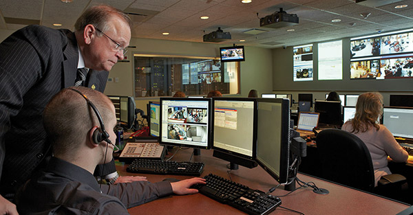 Mike Neugebauer, VP and Director of Corporate Security for Fifth Third Bank, leans over a man sitting at a computer monitor to view video surveillance images on the screen.
