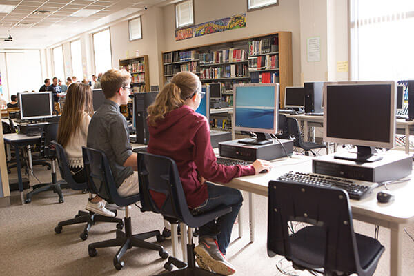 students sit at computers inside a school library