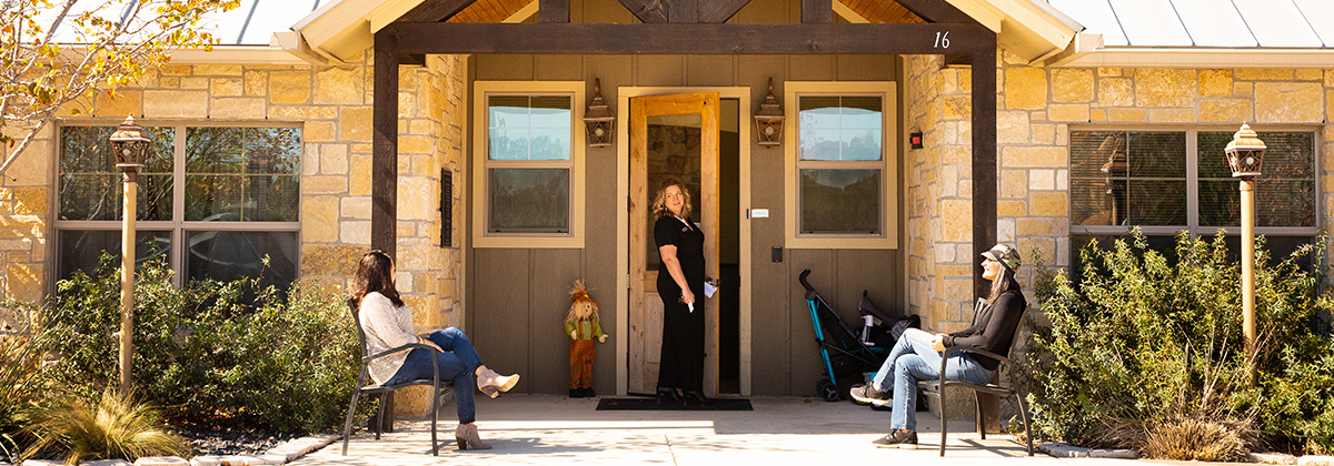 Entrance doors to Kendall County Women’s Shelter with two women sitting on opposite benches and one woman opening the door