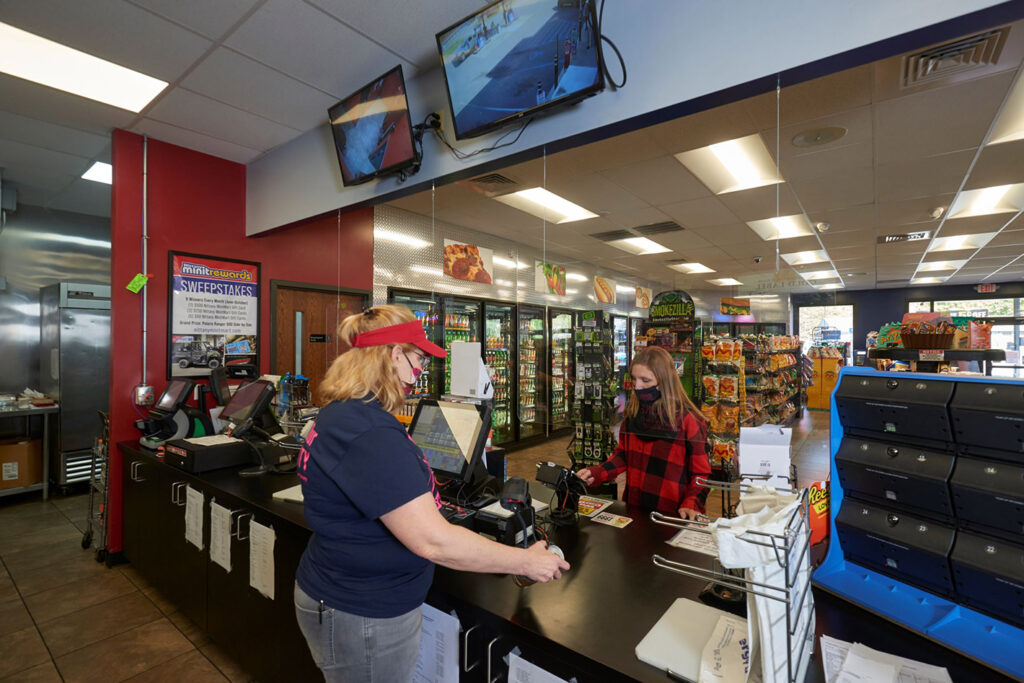 Convenience store cashier helping a customer while the surveillance system is concealed above the service counter.