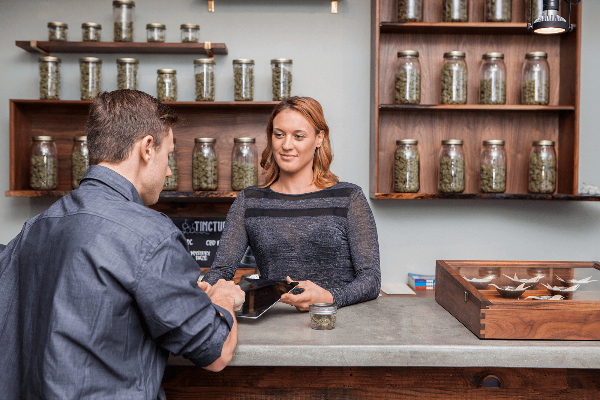 Female holding tablet while male uses it in cannabis dispensary.