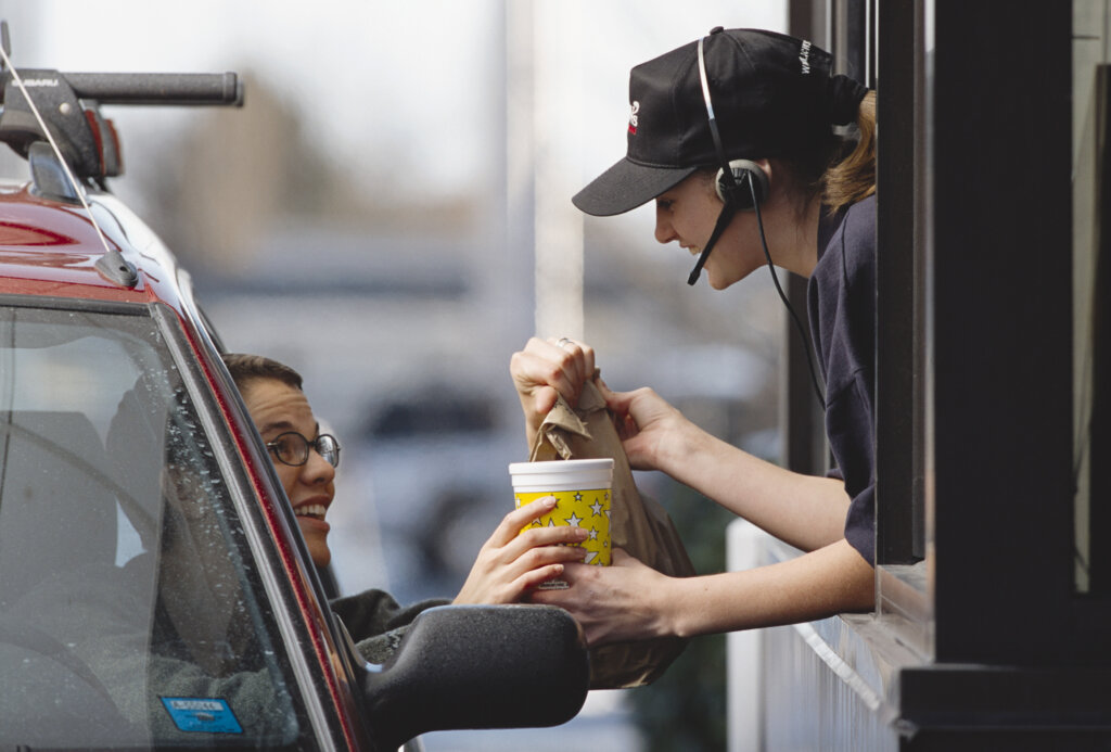 Fast-food restaurant employee hands customer order at drive-thru window
