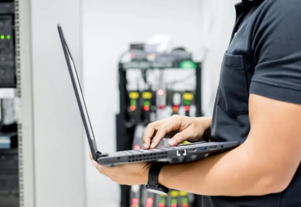Un technicien informatique utilisant un ordinateur portable dans la salle des serveurs pour gérer les systèmes de vidéosurveillance du réseau