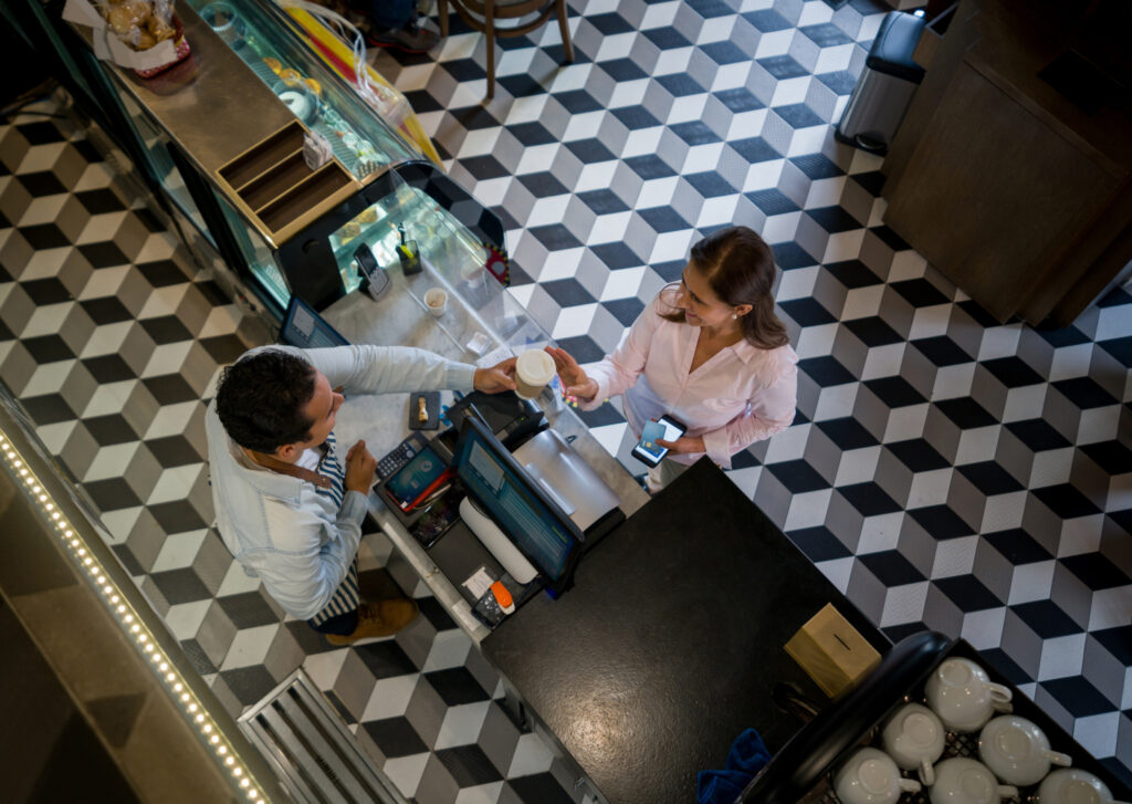 Latin American woman at a cafe buying a cup of coffee to go and paying by credit card - food and drinks concepts.